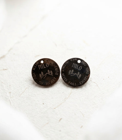Two black dog tags with engraved text on a white textured background