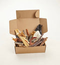 Open cardboard box filled with various dog treats on a white background